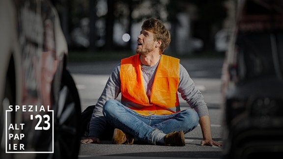 Ein Mann mit Warnweste sitzt vor zwei Autos auf der Straße.