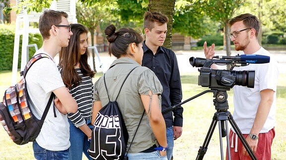 Junger Mann erklärt Jugendlichen eine Kamera.