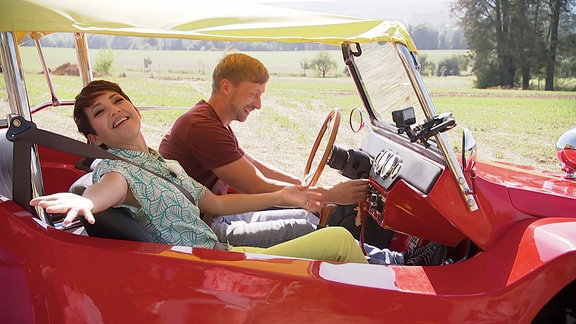 Ein Mann und eine Frau sitzen in einem roten Auto.