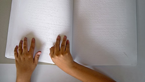 Hände ertasten die Blindenschrift in einem Buch