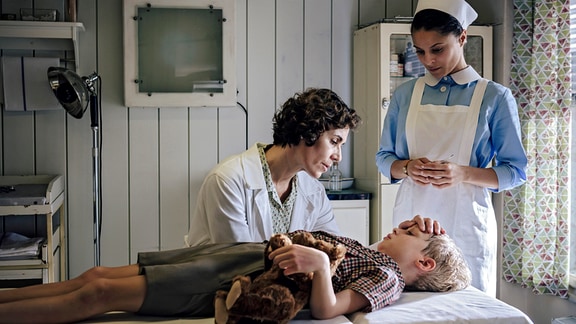 Der kleine Werner (Hugo Gross, M.) wird mit Symptomen von Kinderlähmung in die Charité eingeliefert. Kinderärztin Dr. Ingeborg Rapaport (Nina Kunzendorf, l.) und Schwester Arianna (Patricia Meeden, l.) versuchen den Jungen zu beruhigen.