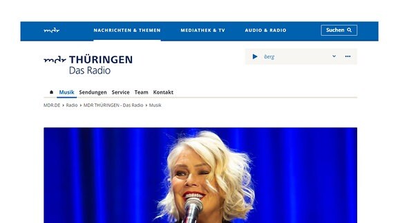 Auf dem Bild ist ein Screenshot von einer Seite auf MDR.de. Zu sehen ist die Seite von "MDR Thüringen - Das Radio". Darauf ist eine Vorschaubild einer Bildergalerie zu sehen. Die Gallerie trägt den Titel "Fotos: Kim Wilde begeistert Fans bei exklusivem MDR-Studiokonzert".