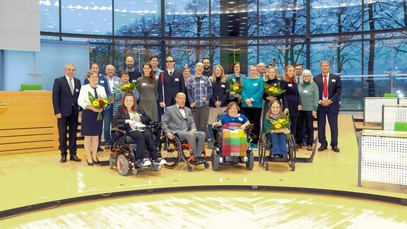 Gruppenbild der Preisträger des Sächsischen Inklusionspreises 2022 im Sächsischen Landtag. In der vorderen Reihe sind vier Personen in Rollstühlen. Die Frauen haben Blumensträusse in der Hand.