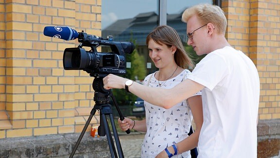 Ein junger Mann erklärt einer jungen Frau eine Video-Kamera.