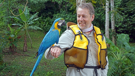 Ein Mann mit einem Papagei auf seinem rechtem Arm.