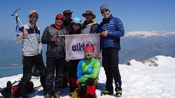 Bergsteiger auf einem Berggipfel mit dem Biwak-Logo