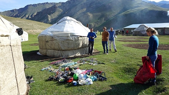Bergsteiger neben Jurten sortieren ihre Ausrüstung in einer gebirgigen Steppenlandschaft