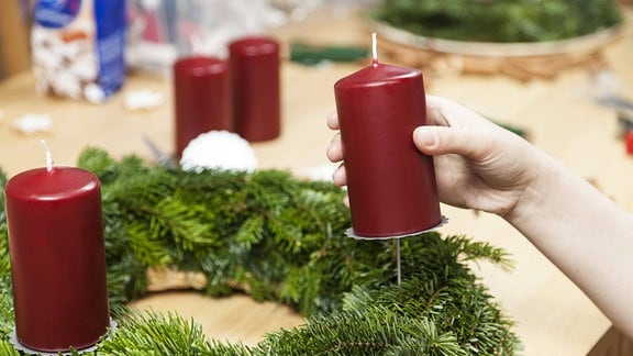 Eine Kerze wird auf einen Adventskranz aufgesteckt.