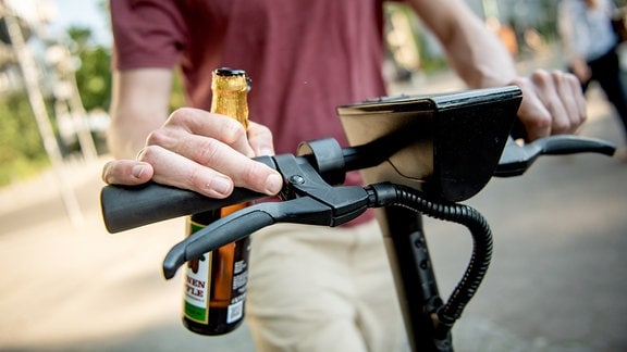 Ein junger Mann mit Bierflasche auf einem E-Roller