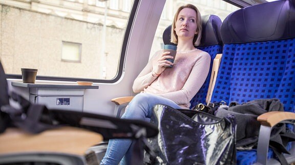 Eine Frau sitzt in einer Regionalbahn in Hamburg und trinkt einen Kaffee (gestellte Szene). 