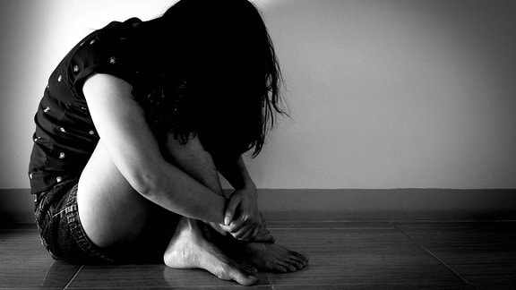 Symbolfoto Missbrauch: eine Frau sitzt verängstigt auf dem Boden