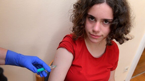 Ein Mädchen blickt in die Kamera und bekommt dabei eine Corona-Impfung.