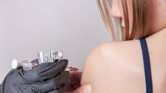 Eine Person mit Schutzhandschuhen indiziert mit einer Impfspritze eine Impfdosis mit dem mRNA-Impfstoff Comirnaty