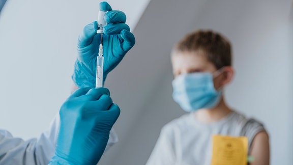 Arzt füllt Spritze mit COVID-19-Impfstoff für Jungen im Hintergrund in einer Klinik