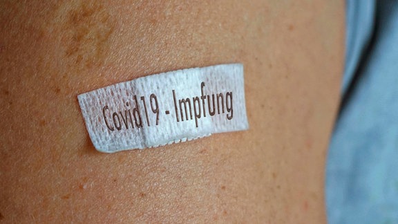Ein kleines Pflaster mit der Aufschrift Covid19-Impfung klebt auf einem Arm.