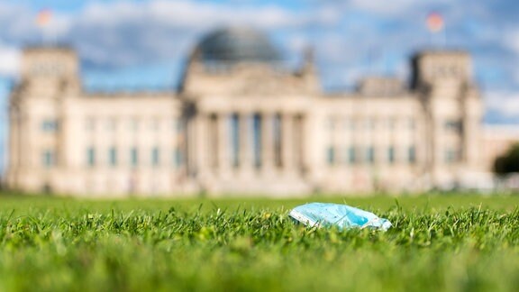 Im Bild ist eine Einwegmaske auf der Wiese vor dem Reichstagsgebäude zu sehen. 