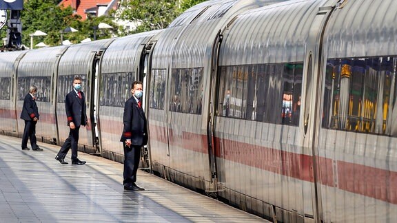Zugbegleiter der Deutschen Bahn tragen Gesichtsmasken am Bahnsteig kurz vor der Abfahrt eines ICE Zugs