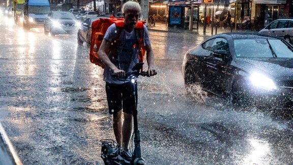 Ein E-Scooter Fahrer fährt bei starkem Regen.