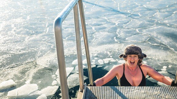 Frau mit Pelzmütze steigt Leiter zu gefrorenem Wasser in hinab 