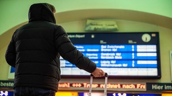 Ein Reisender steht in einem Bahnhof und schaut zur Anzeigetafel