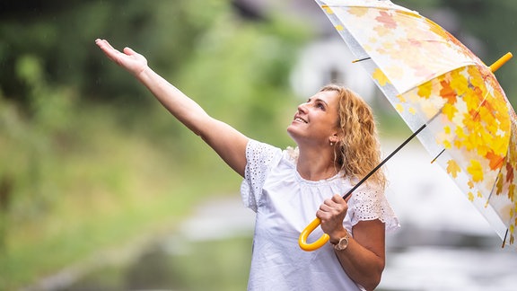 Eine Frau unter einem Regenschirm streckt die Hand aus.