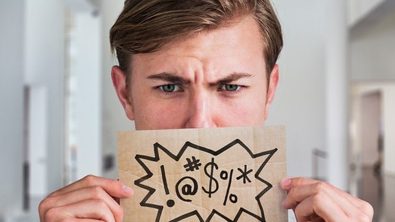 Symbolbild: Ein Mann hält einen Zettel vor seinen Mund.