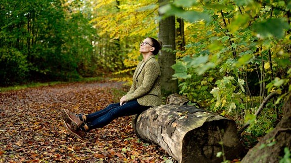 Frau sitzt in einem herbstlichen Wald auf einem Baustamm