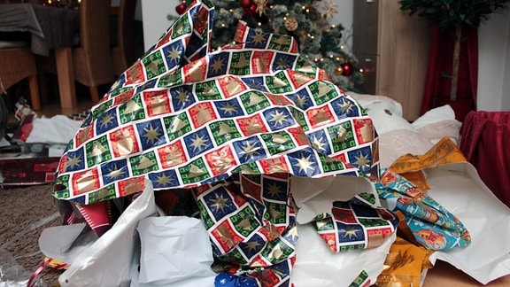 Geschenkpapier ausgepackter Weihnachtsgeschenke türmt sich vor einem Weihnachtsbaum 