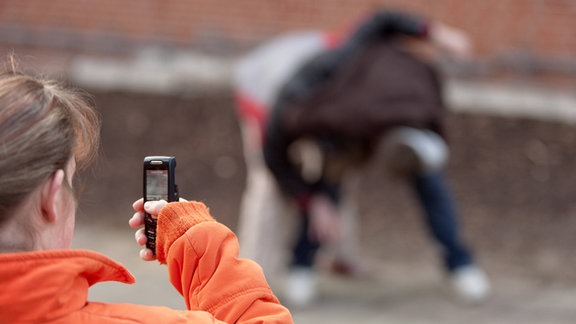 Zwei Jungen prügeln sich auf dem Schulhof und werden dabei von einem Mädchen mit ihrem Handy gefilmt.