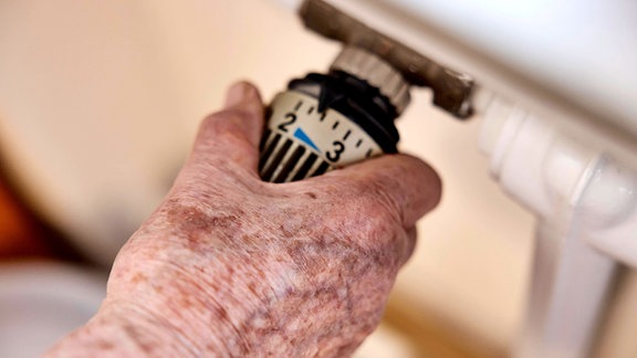 Hand einer Seniorin mit Altersflecken auf dem Thermostat einer Heizung