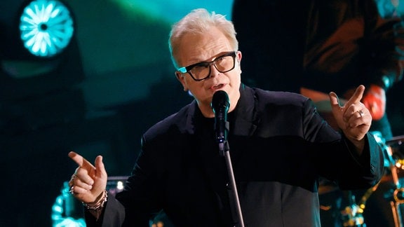 Herbert Grönemeyer, ein Mann mit grauen Haaren und Brille singt auf einer Bühne