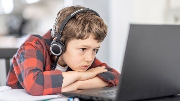 Junge schaut konzentriert auf Laptop.