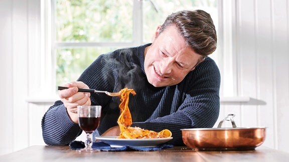 Jamie Oliver ist ein Gericht an einem Tisch bei einem Glas Rotwein.