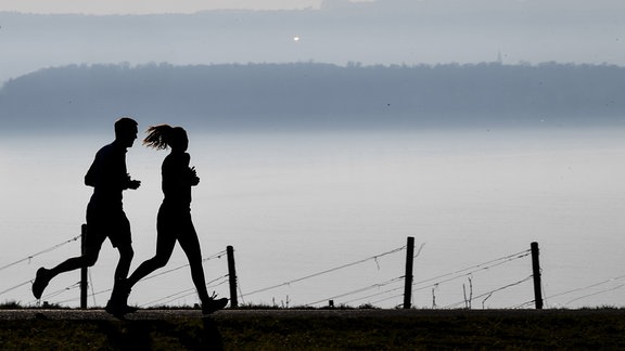 Die Silhouetten von joggenden Personen sind vor einer nebeligen Landschaft zu sehen