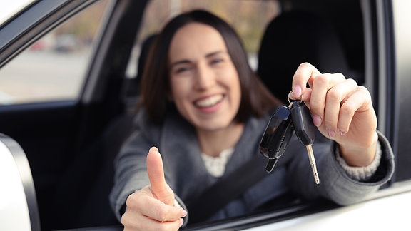 Eine Frau zeigt aus einem geöffneten Pkw-Fenster einen Autoschlüssel