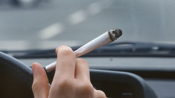 Ein junger Autofahrer raucht einen Joint während der Autofahrt. 