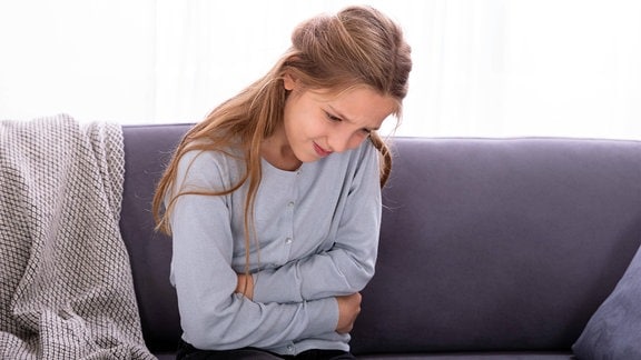 Mädchen mit Bauchschmerzen auf Sofa