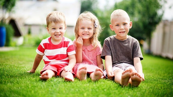 Ein Mädchen und zwei Jungen sitzen auf einer Wiese