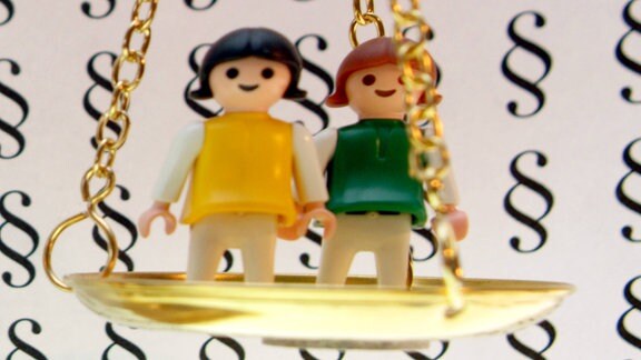 Zwei Playmobil-Figuren stehen auf einer Waagschale.