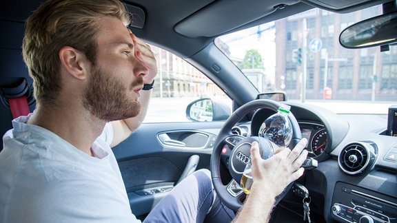 Ein Mann fast sich beim Autofahren an den Kopf.