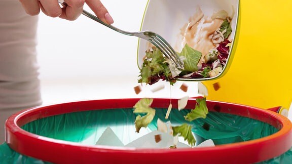 Eine Frau schmeißt einen Salat in den Müll