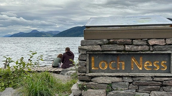 Menschen sitzen am Ufer des Loch Ness