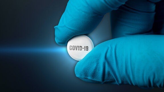 Tablette mit der Aufschrift "Covid-19" wird von einer Hand im Handschuh gehalten.