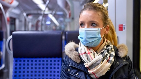 Frau mit Mundschutzmaske sitzt in Zug