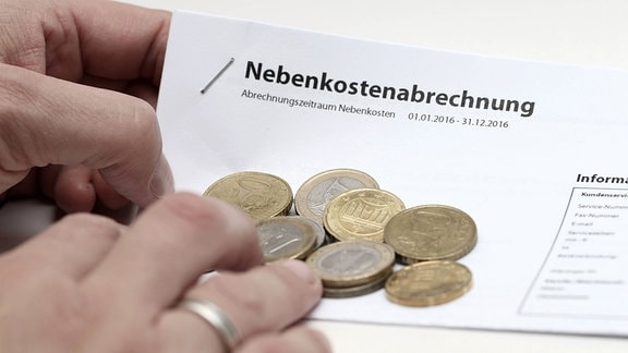 Hand hält Nebenkostenabrechnung mit Euro Münzen.