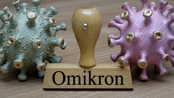 Coronamodelle und ein Stempel mit Omikron Schriftzug liegen nebeneinander.