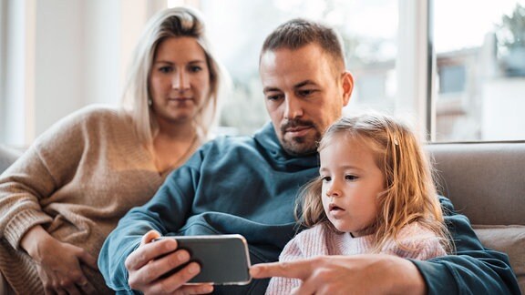 Vater, Mutter und Kind schauen aufs Handy.