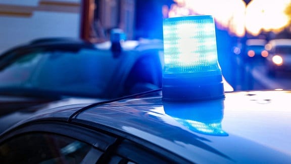 Eingeschaltetes Blaulicht auf dem Dach eines zivilen Polizeifahrzeuges in der Dämmerung.