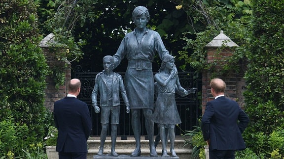 Prinz William und Prinz Harry steheh vor einer Statue mit ihnen und ihrer Mutter, Lady Diana. 