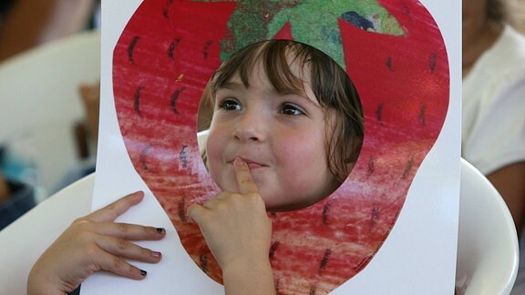 Kind schaut durch Bild, das eine Erdbeere mit einem großen Loch zeigt.